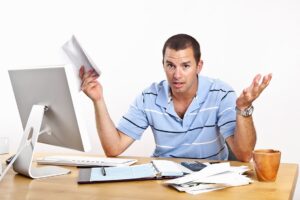 Frustrated man holding bills at computer