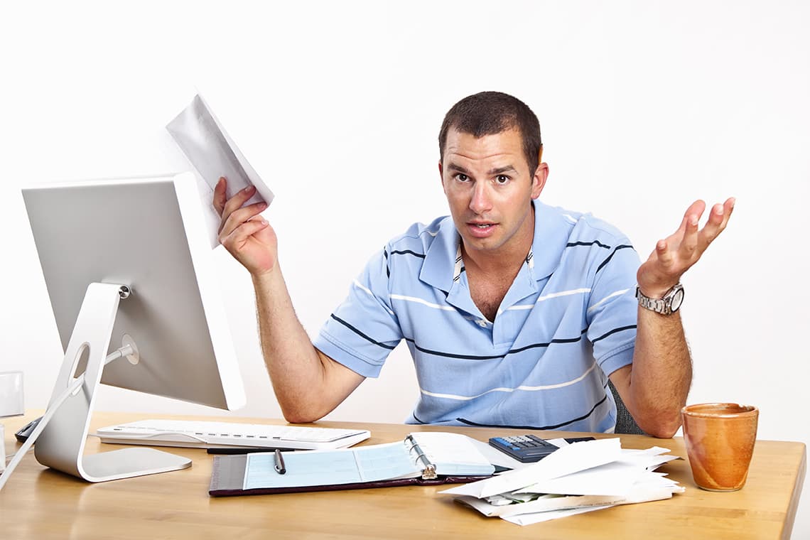 Frustrated man holding bills at computer